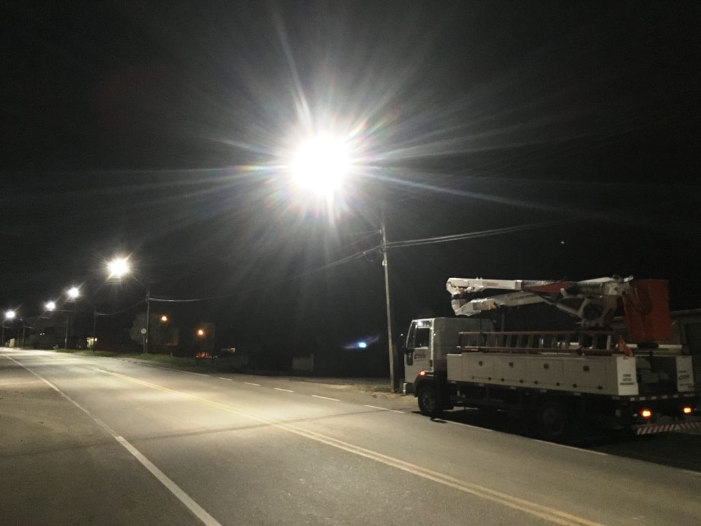 Foto de uma rua em Campo Largo, destacando os postes de iluminação pública com as luzes acesas. No canto direito da imagem aparece o caminhão de serviços da Cocel estacionado.